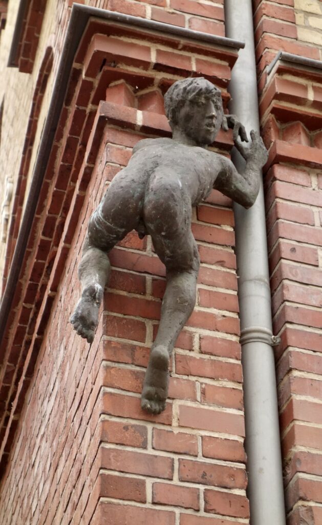 Eine nackte Figur klettert an einem Abflussrohr in Stralsunds Altstadt